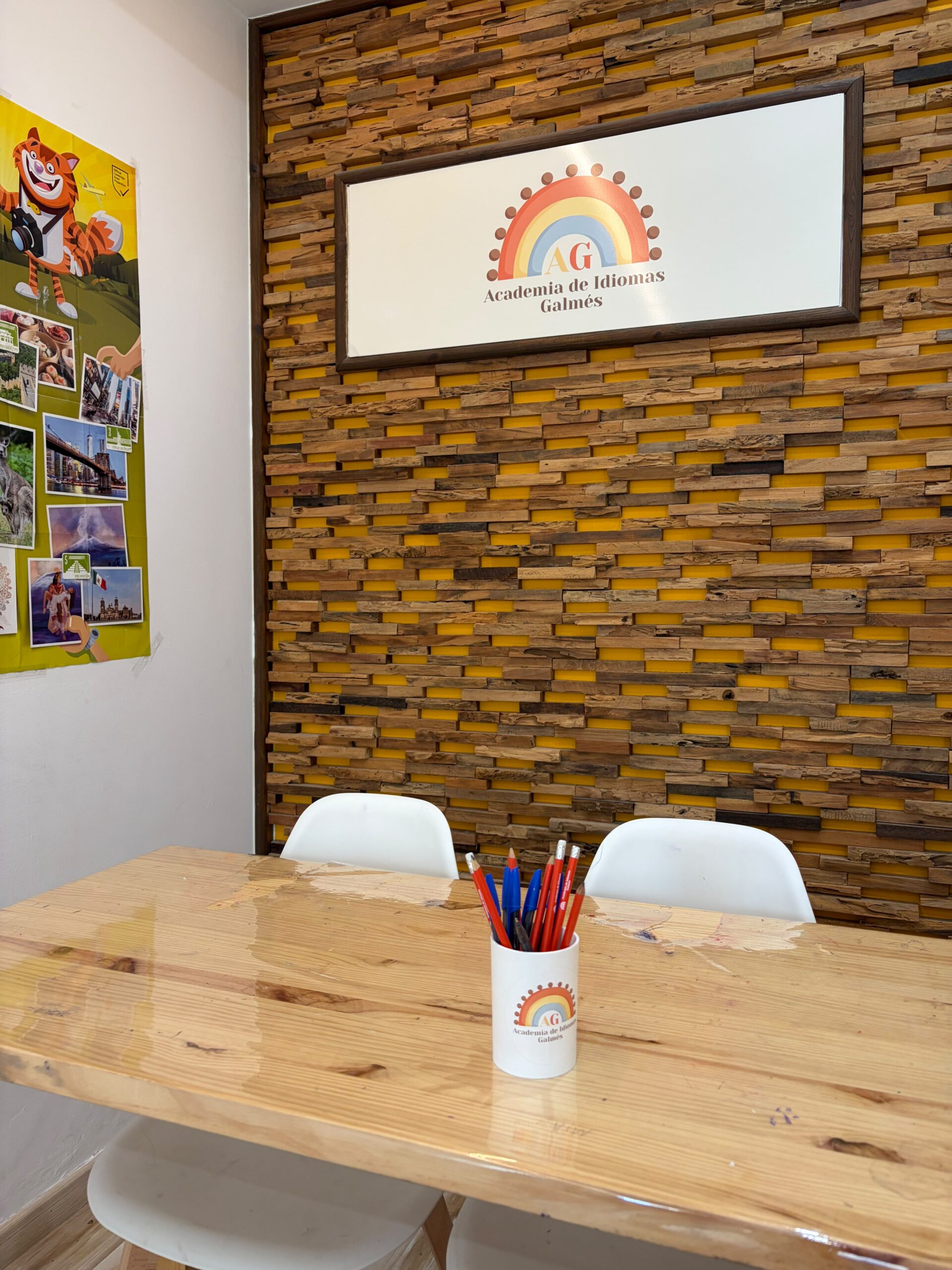Mesa con lápices y el logo de la academia en la pared de madera