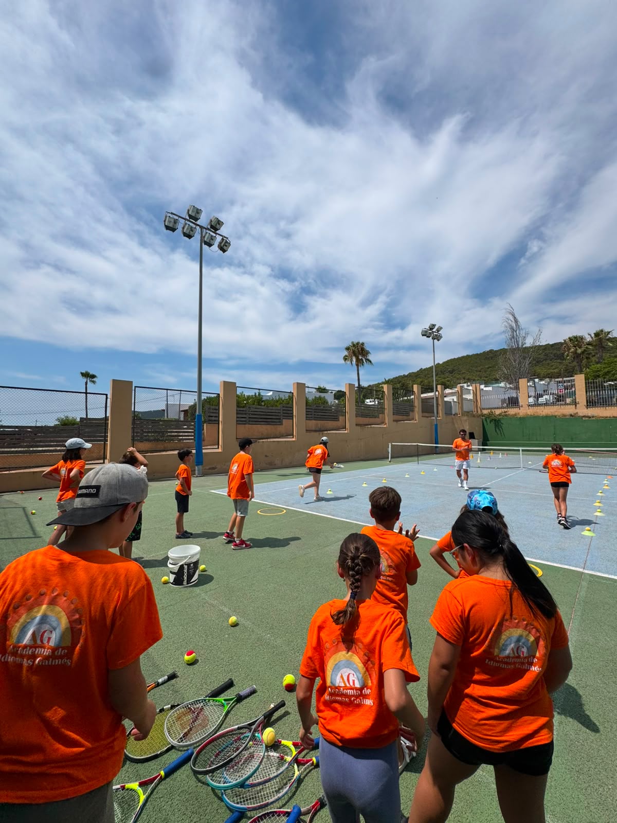 Alumnos con camiseta de la academia en una pista de tenis